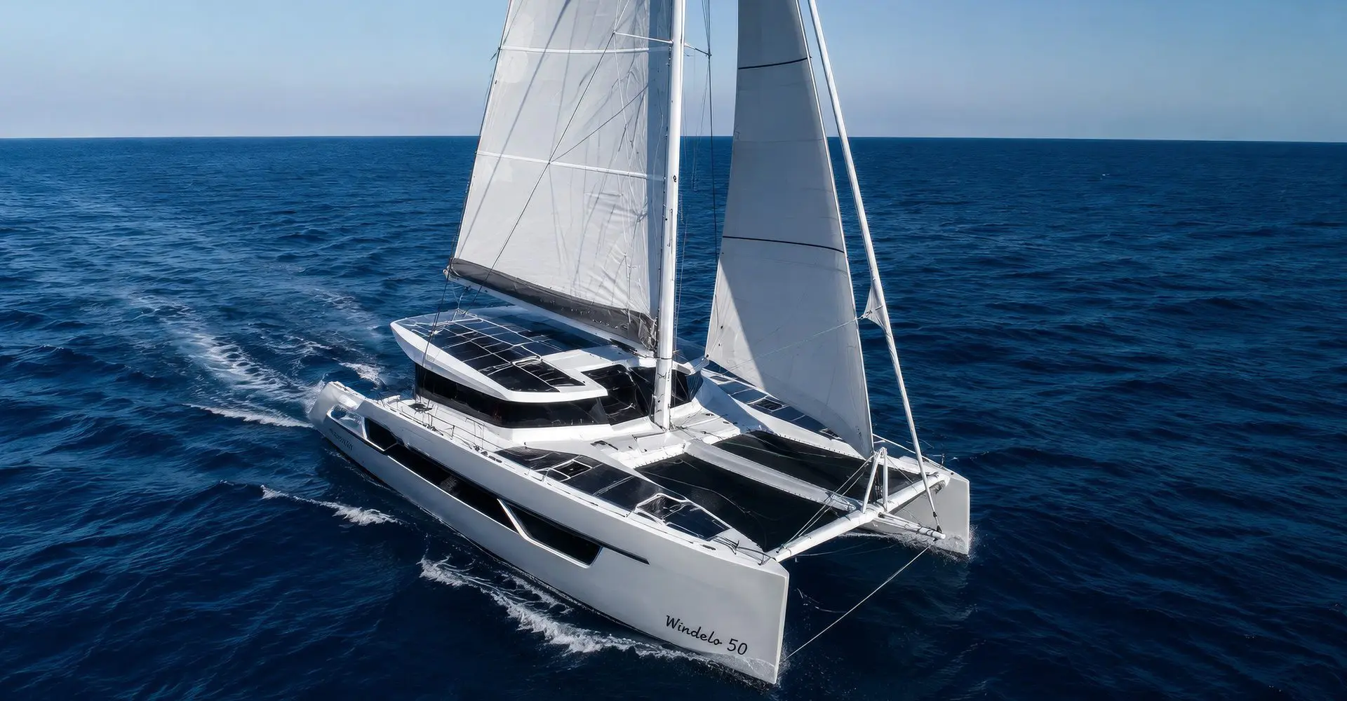 Electric performance catamaran sailing under full main and jib on open ocean, solar panels on deck, wake astern