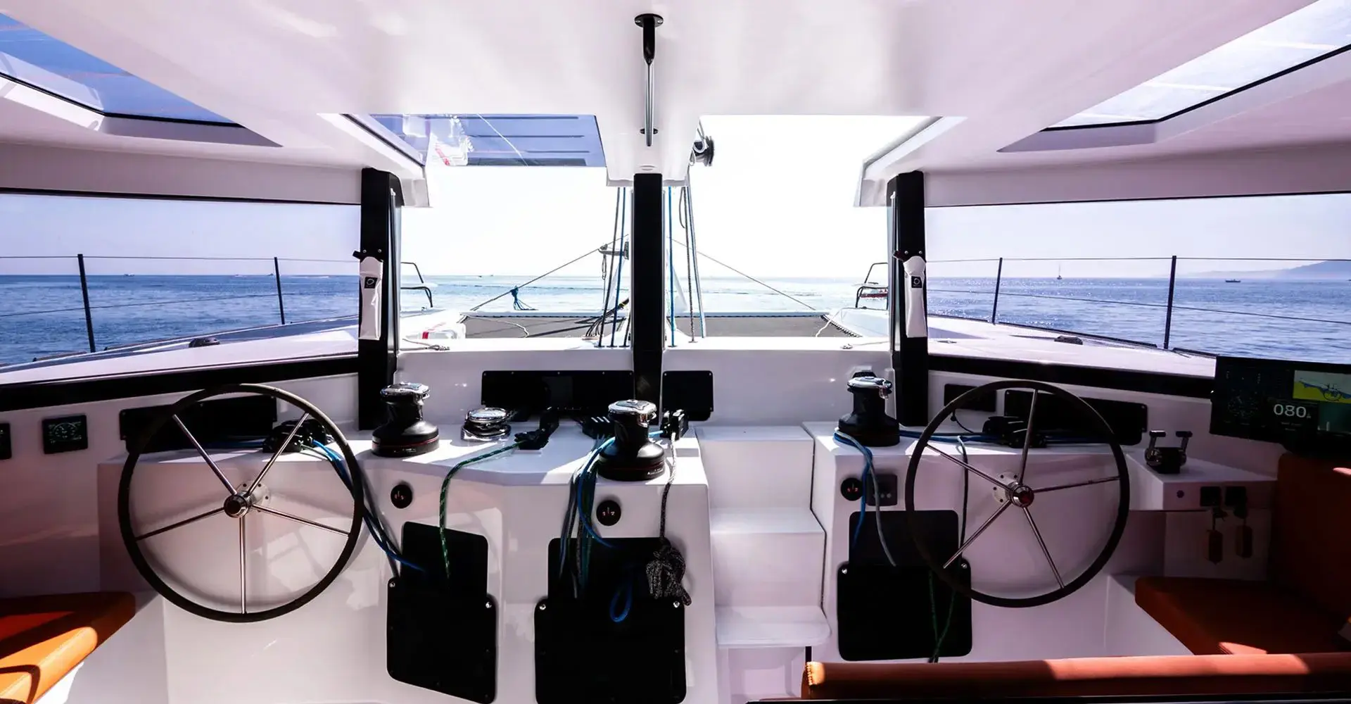 Twin helm stations of a performance catamaran with steering wheels, winches and instruments, open sea view aft